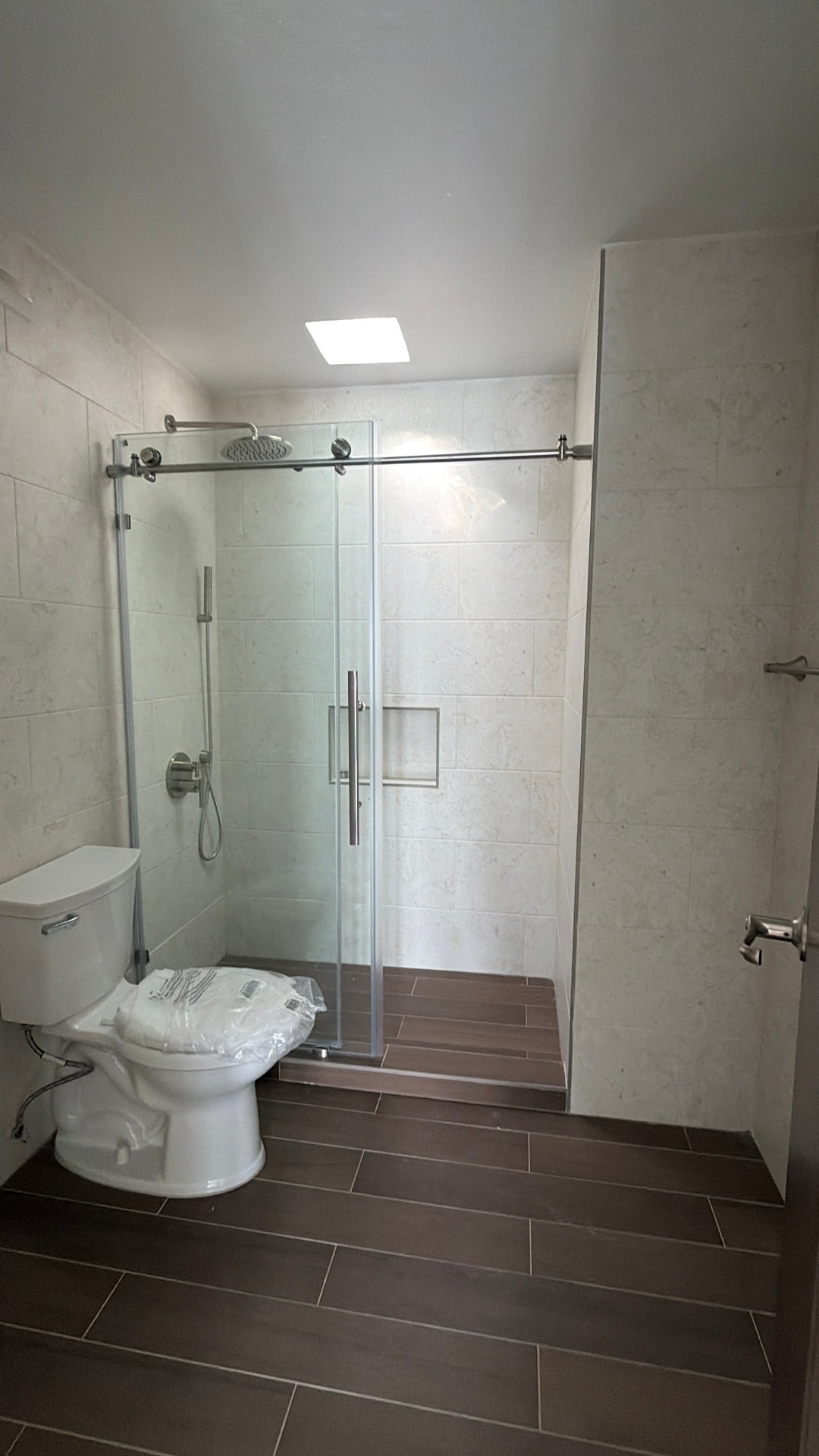 Baño remodelado con ducha de cristal, losa de mármol y piso tipo madera